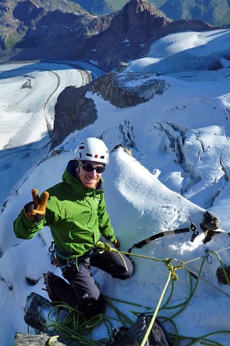 Angeseilter Hochtourengeher mit Hochtourenausr&uuml;stung lacht in die Kamera und macht ein Piece-Zeichen.