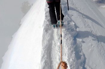 Bergsteiger-Füße in einer schmalen Schneespur auf einem Gratweg.