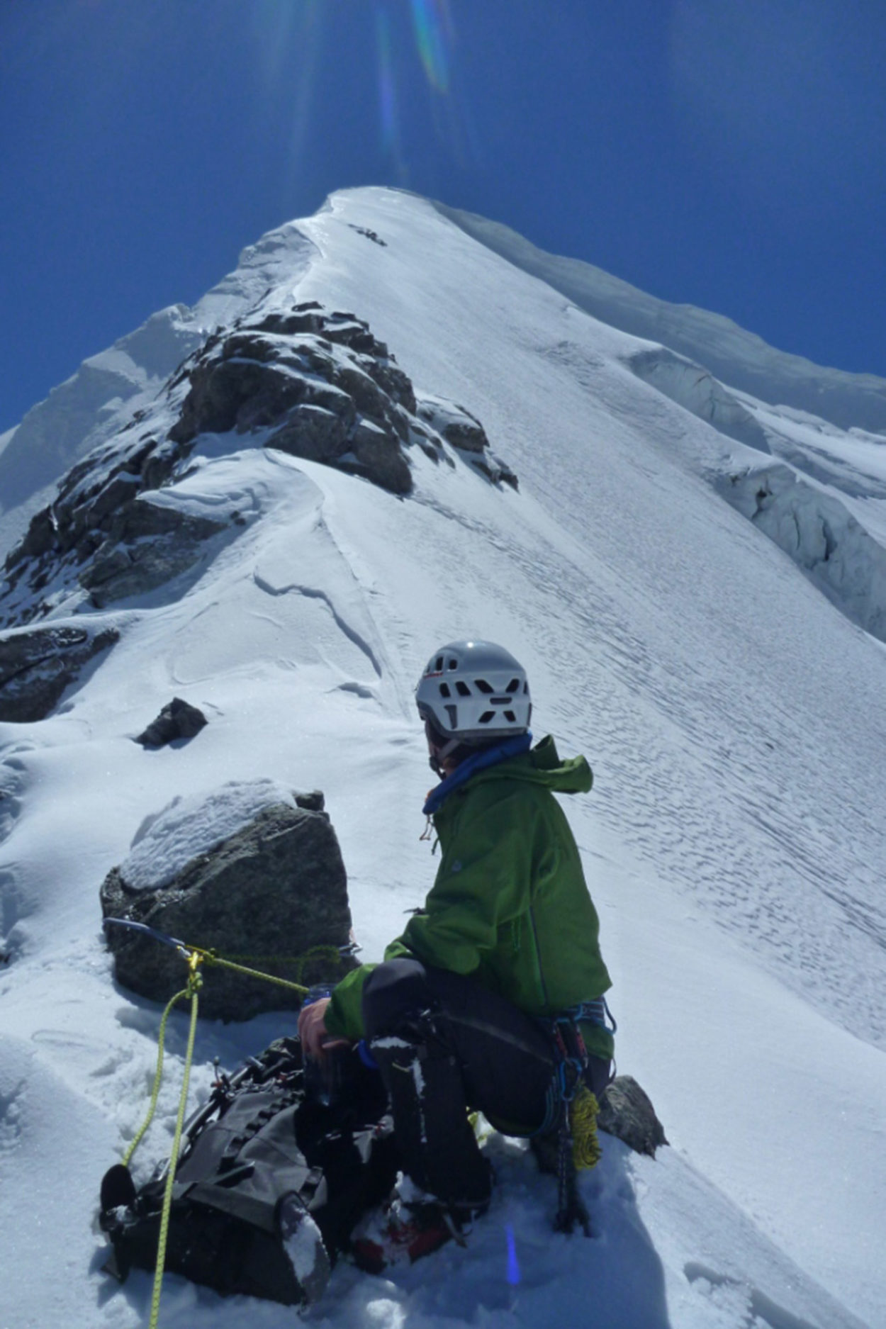 Hochtourengeher sitzt am Gipfelgrat, sichert mit einem Seil den Nachgeher und schaut in Richtung Gipfel des Piz Pal&uuml;.
