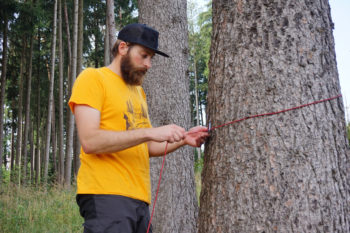 Abbildung 1: Lege die Firstschnur mit einem Karabiner um einen Baum und hänge den Karabiner anschließend in die Schnur ein. Foto: Flo Glott