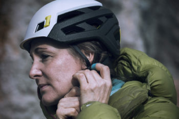 Eine Frau mit dem Mammut Wall Rider MIPS Kletterhelm auf dem Kopf verstellt das Gurtband mit der Hand.