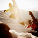 Zwei Bergsteiger mit Ski am Rücken steigen mit Pickel einen schneebedeckten Hang hinauf