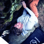 Ein Boulderer am Fels mit Crashpad im Hintergrund