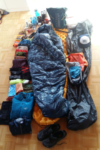 Ausrüstung und Bekleidung fürs Backpacking ist auf dem Fußboden ausgebreitet
