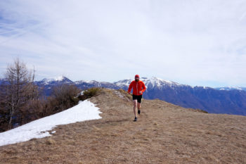 Trailrunner läuft auf Bergwiese auf die Kamera zu