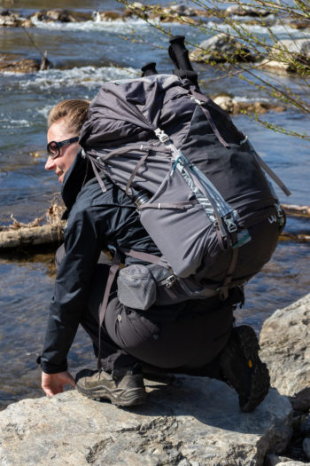Frau mit Gregory Maven auf dem R&uuml;cken kniend am Fluss