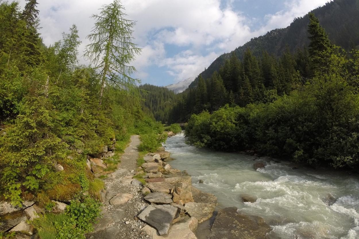Ein wilder Fluss in Berglandschaft, daneben ein Weg.