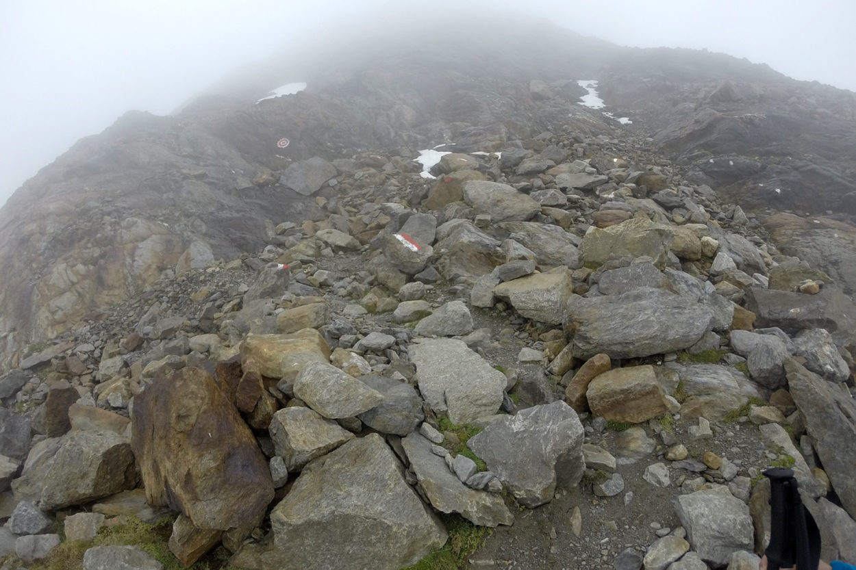 Geröll und Steine mit einer rotweißen Markierung im Nebel.