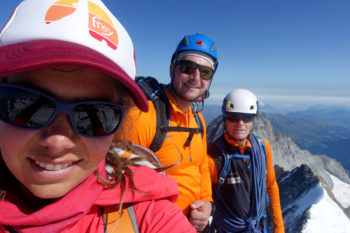 Drei Bergsteiger schauen in die Kamera auf einem Berggipfel.