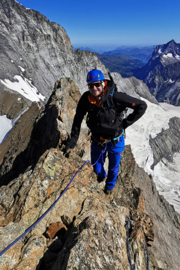 Ein Bergsteiger am Seil von oben auf einem Felsgrat.