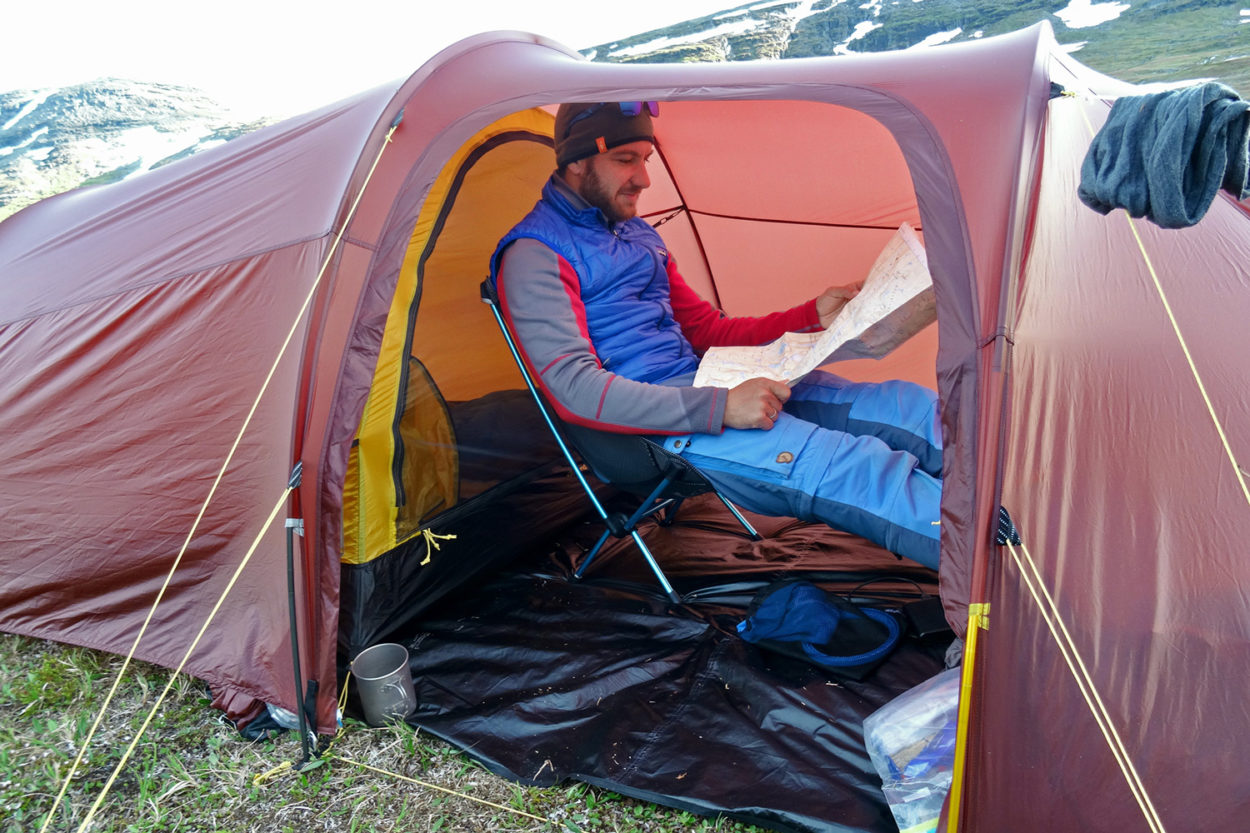 Ein Mann sitzt in der Apsis des Zeltes auf einem Faltstuhl und hat eine Karte ausgebreitet.