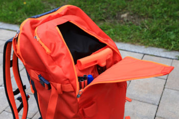 Oranger Rucksack mit geöffnetem Frontfach, in dem sich eine Lawinenschaufel befindet.