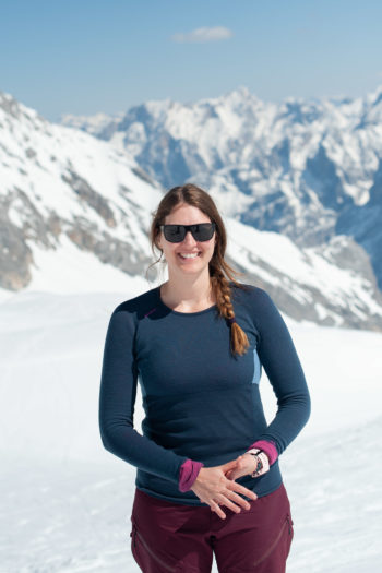 Frau vor Bergpanorama hält sich die Hände und trägt Devold Shirt