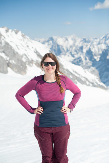 Frau vor Bergpanorama lacht in die Kamera und trägt Merinoshirt