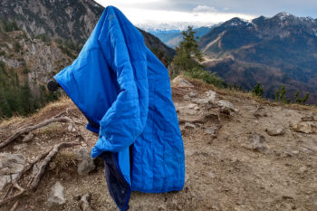 Die Icebreaker Hyperia Lite Hybrid Jacke h&auml;ngt auf einem Ast am Berg.